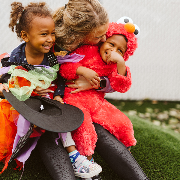 mother holding two toddlers on her lap, the children are wearing sesame street costumes