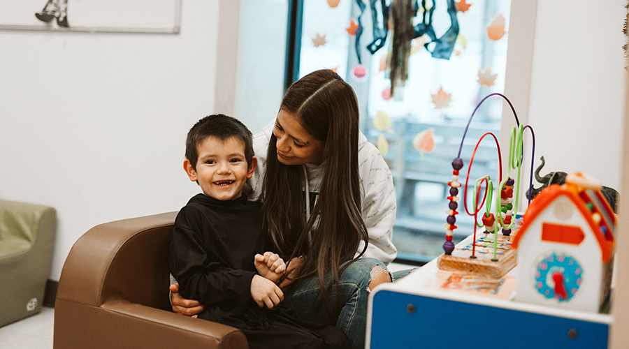 mother holding son close as they sit in front of a table with children's toys on the surface, they are both smiling
