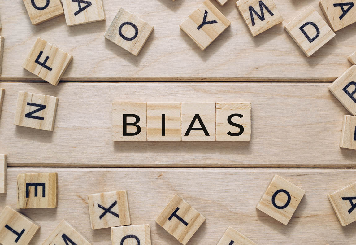 Wooden tiles arranged to spell the word bias on a light wooden background with additional scattered letters creating a thoughtful atmosphere