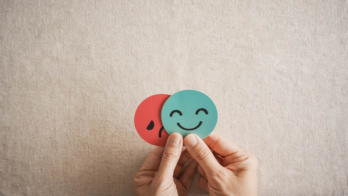 Hands holding sad face hiding behind happy face, bipolar and depression, mental health, split personality, mood change concept